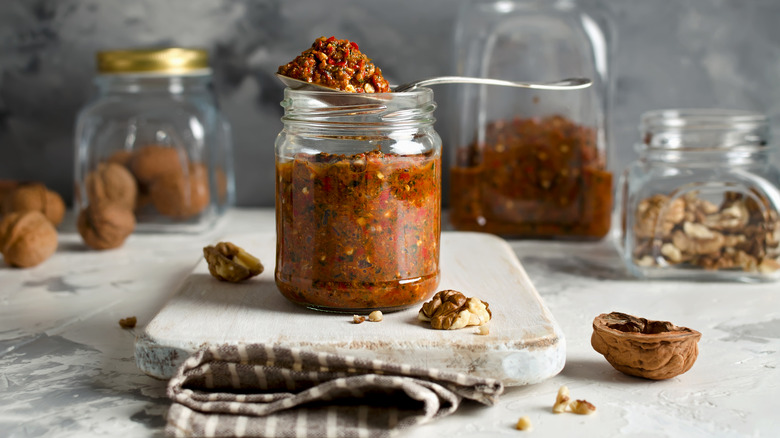 Glass jar full of walnut-based condiment surrounded by whole walnuts and pieces of walnuts in jars