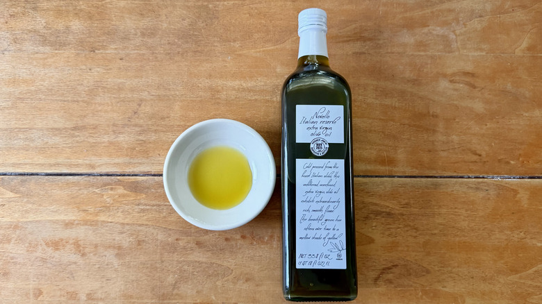 a bottle and white sauce dish of Trader Joe's Novello Italian Reserve Extra Virgin Olive Oil on a wooden table