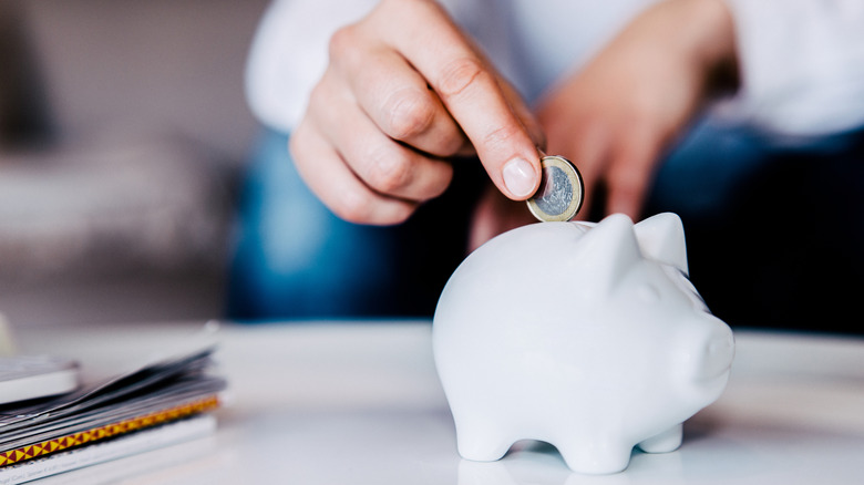 hand adding coin to a piggy bank