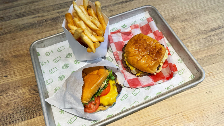 Two smash burgers on a tray with a carton of French fries