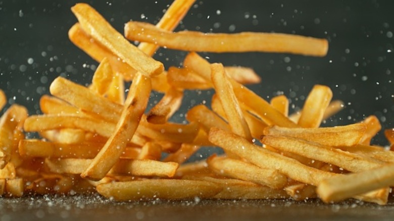 Salted french fries being dropped onto a surface