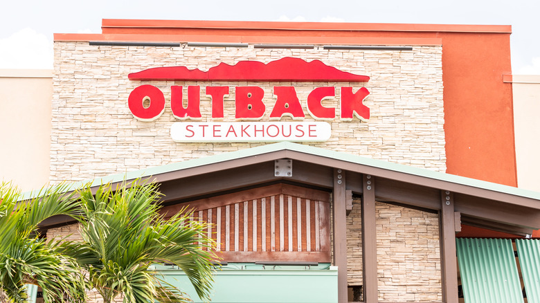 The exterior with an Outback Steakhouse with palm trees in the foreground
