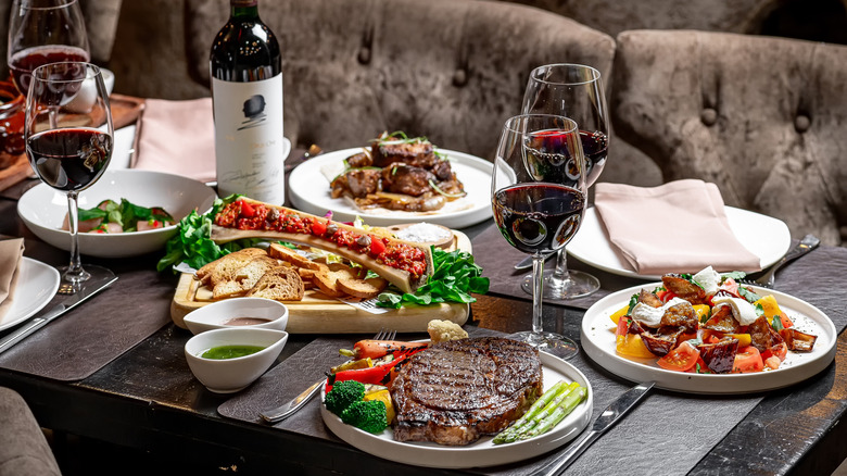 A table at a steakhouse featuring wine, steak, assorted dishes
