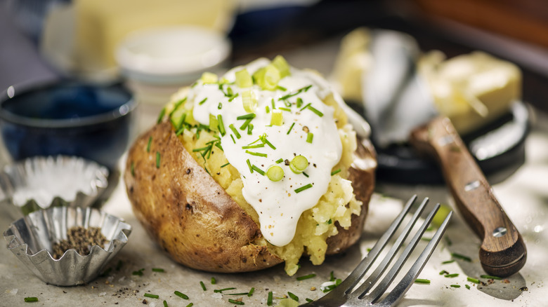 A loaded baked potato with sour cream and herbs on a platter