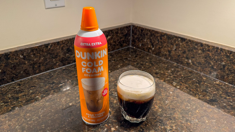 Dunkin' cold foam creamer on counter next to a glass of coffee with creamer on top