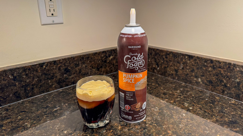 Pumpkin spice cold foam creamer in the canister next to a cold brew topped with creamer