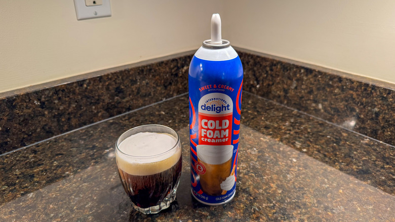 International Delight cold foam creamer canister with a glass of coffee next to it