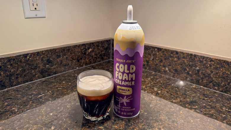 Trader Joe's vanilla cold foam creamer canister next to cold brew in a glass with creamer on top