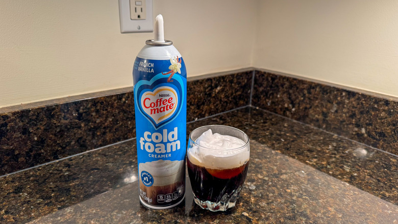 Cold foam on top of iced coffee with the canister next to it on a kitchen counter