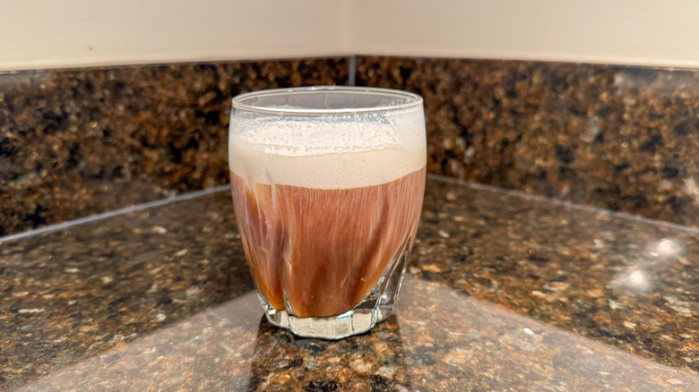 A glass of coffee with cold foam on top on a countertop