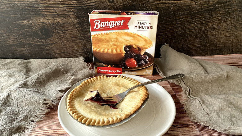 A Banquet individual cherry pie on a plate with a fork in it in front of the box