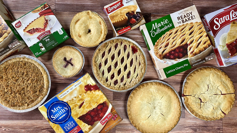 Assorted whole cherry pies next to their boxes on a wooden table