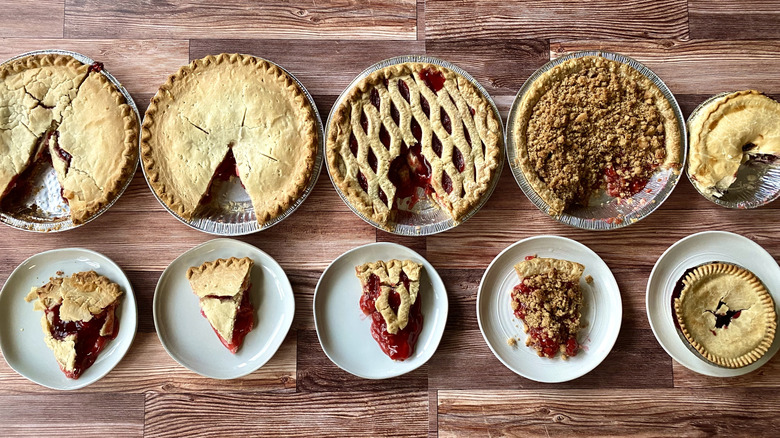 Whole cherry pies with a slice cut out of each of them on separate plates on a wooden table