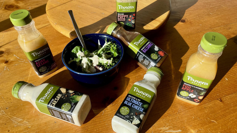 Bowl of salad with various Panera salad dressings around on wooden table