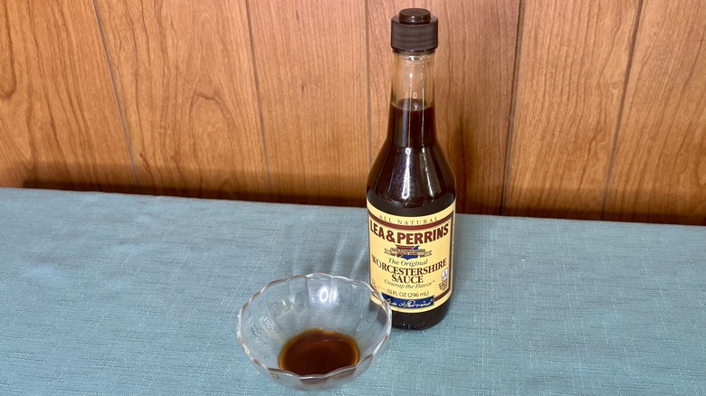 A small glass dish with Worcestershire sauce covering the bottom - a bottle of Lea & Perrins original Worcestershire Sauce stands behind the dish
