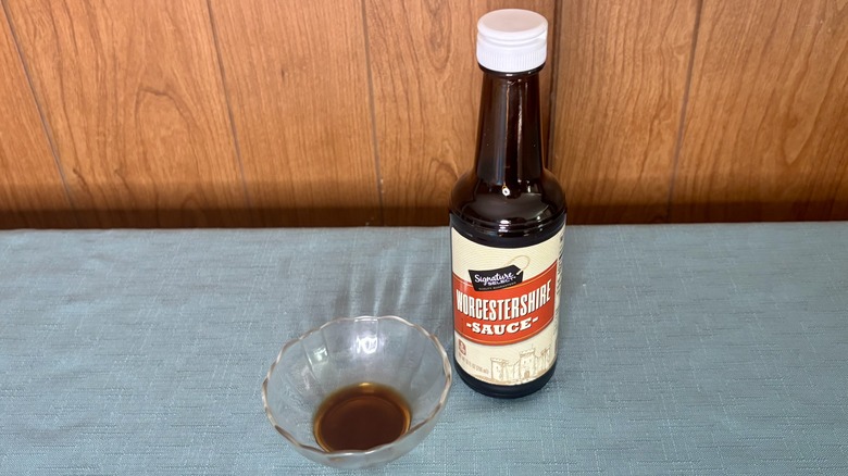 A small glass dish with Worcestershire sauce covering the bottom - a bottle of Signature Select Worcestershire Sauce stands behind the dish