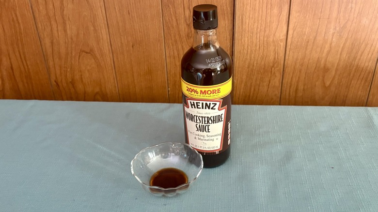 A small glass dish with Worcestershire sauce covering the bottom - a large bottle of Heinz Worcestershire Sauce stands behind the dish