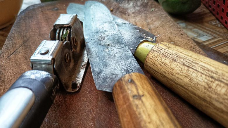 Two vintage carbon steel knives next to a knife sharpener on a wooden table