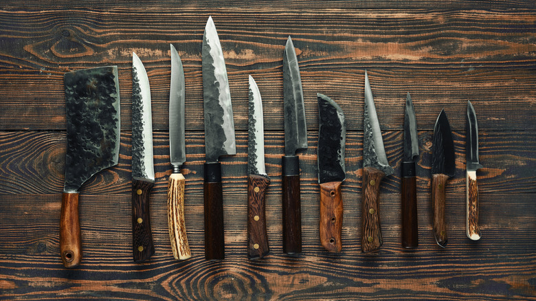 An array of hand-hammered high-carbon kitchen knives on a dark wooden table