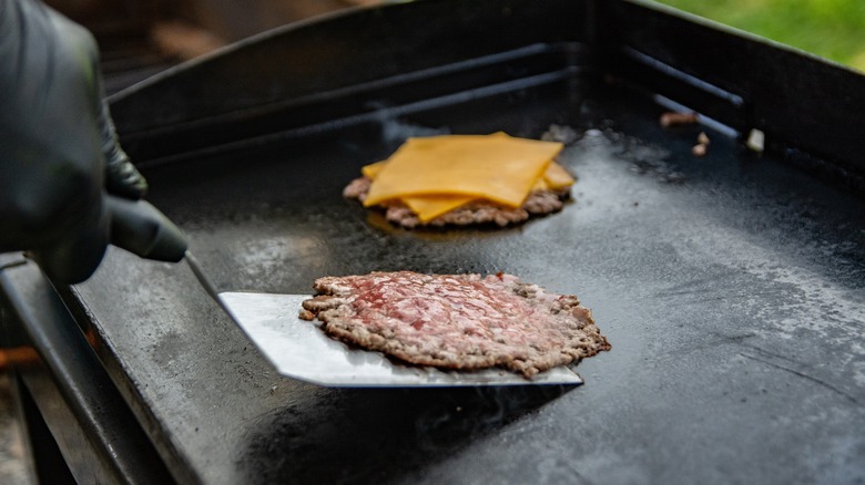 a person flipping a smash burger on a griddle