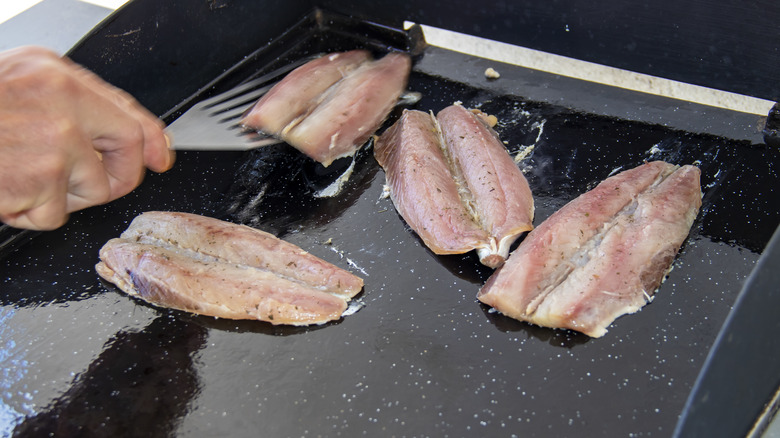 a person flipping a fish filets on a griddle