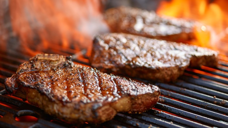 Three steaks over fire on a grill