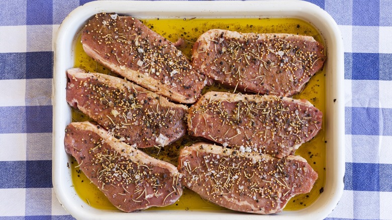 Six steaks sitting in a dish with marinade