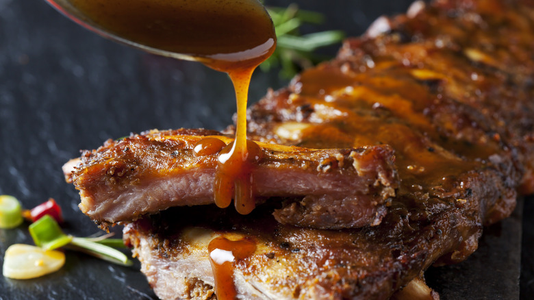 A spoon drizzles a sauce onto a well seasoned rack of ribs