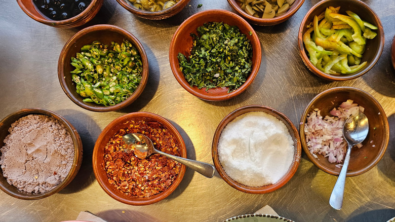 Several different spices in small brown bowls two with spoon within