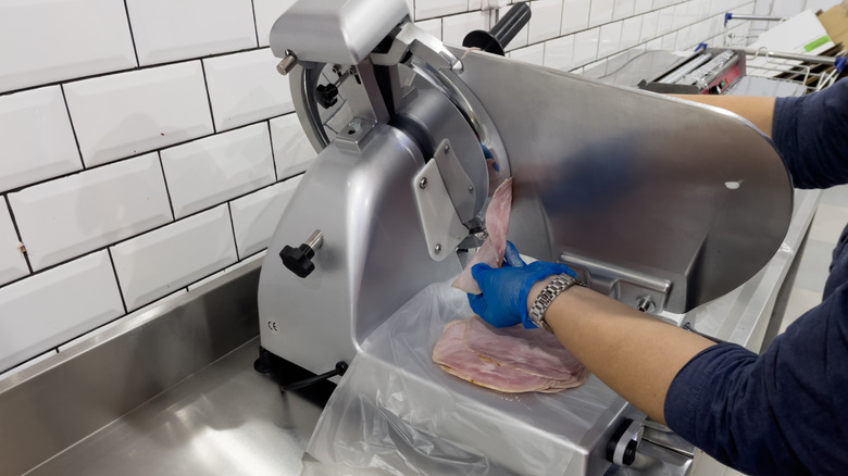 Person slicing ham at a deli