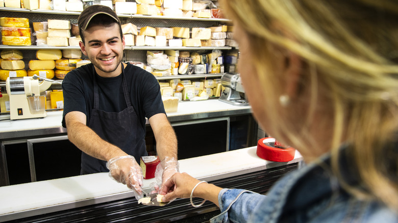 Deli employee giving customer cheese sample