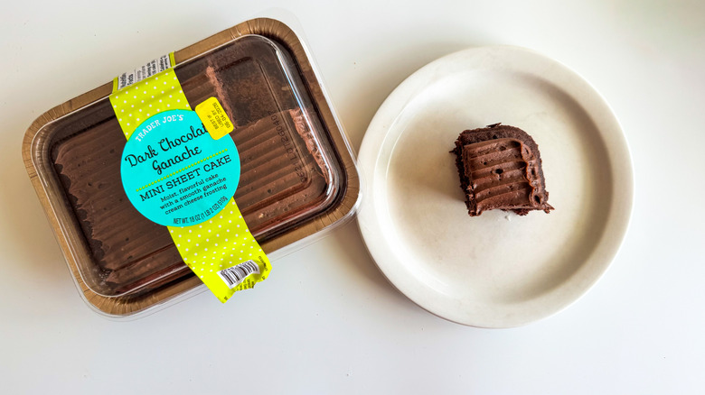 A dark chocolate mini sheet cake with packaging next to a small piece of cake on a plate on a white surface