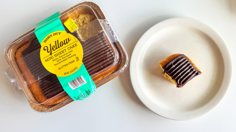 Trader Joe's yellow sheet cake in a plastic container with a small piece on a white plate against on a white background
