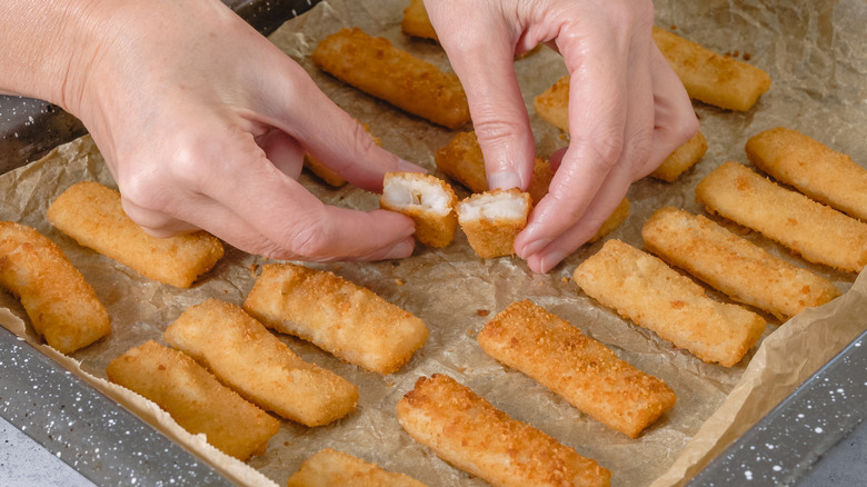 Someone placing fish sticks on a parchment-lined baking sheet