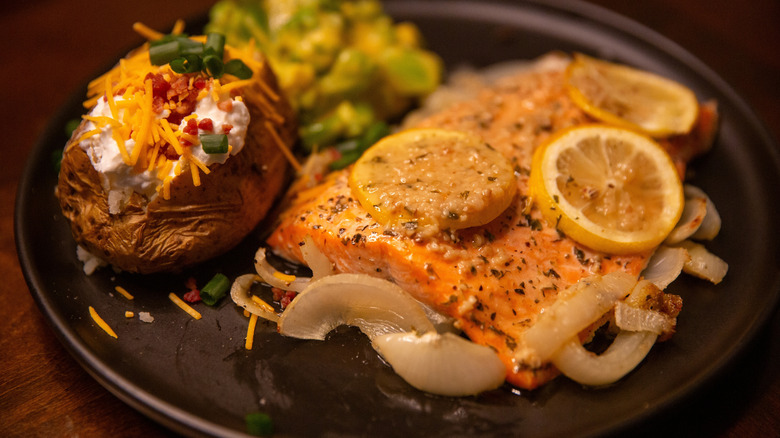 Baked steelhead trout and a baked potato on a black plate
