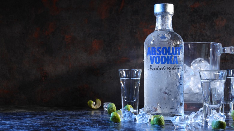 A bottle of Absolut vodka with shot glasses, ice, and lime swirls