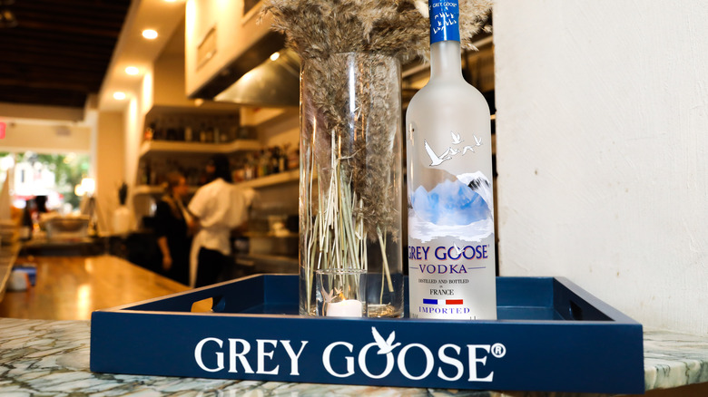 A Grey Goose vodka bottle next to a vase of dried flowers