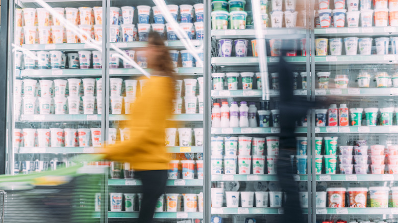 Two blurred figures passing each other in the refrigerated aisle of the grocery store.