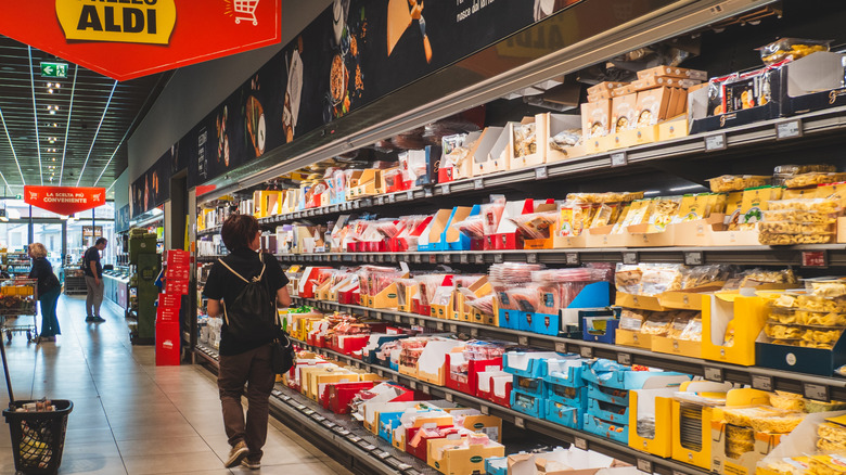 Woman wearing dark clothes and backpack walking down an aisle of refrigerated foods at Aldi in Italy