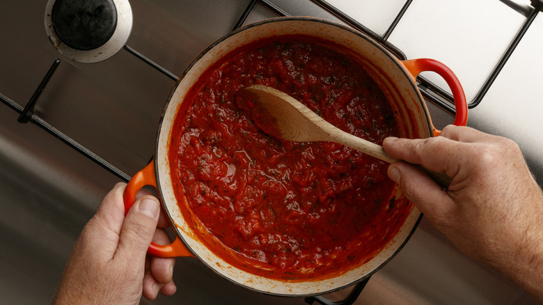 a man stirring a tomato sauce in a dutch oven