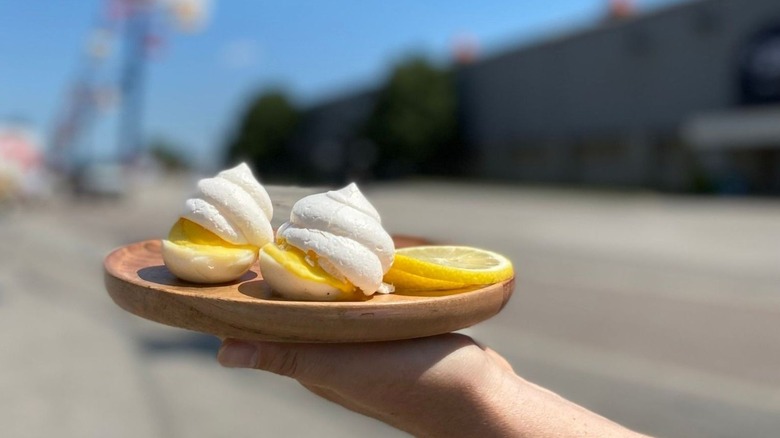 a hand holding lemon meringue eggs on a wooden plate