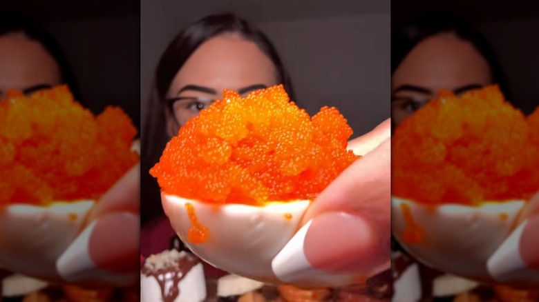 woman holding an egg with fish eggs in front of her face