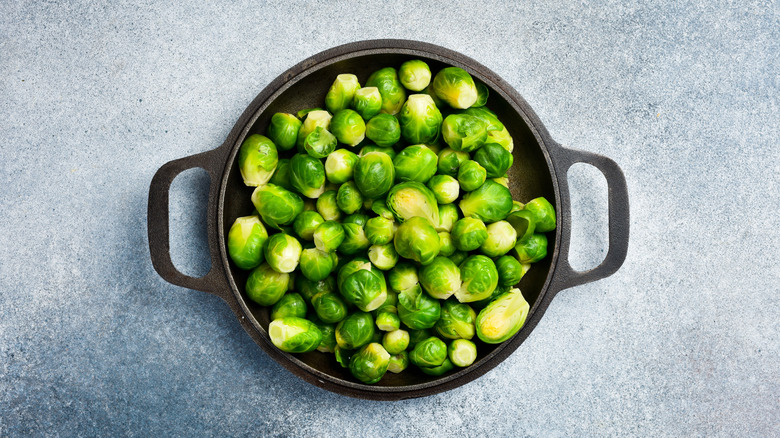 Cast-iron pan filled with bright green Brussels sprouts on a blue background