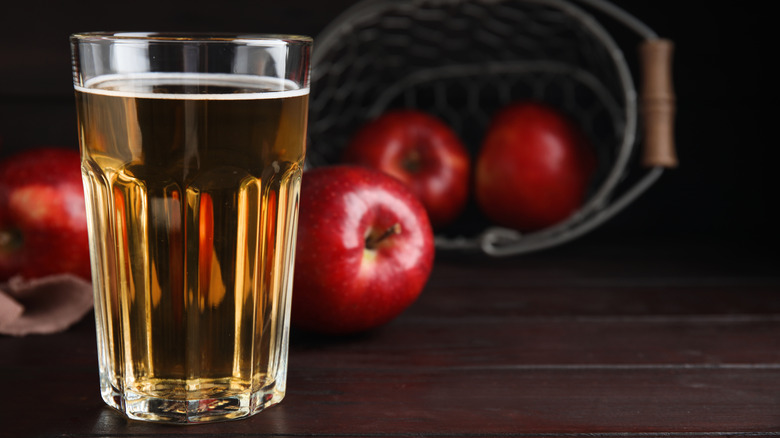 A glass of apple cider in front of a spilled basket of luscious red apples