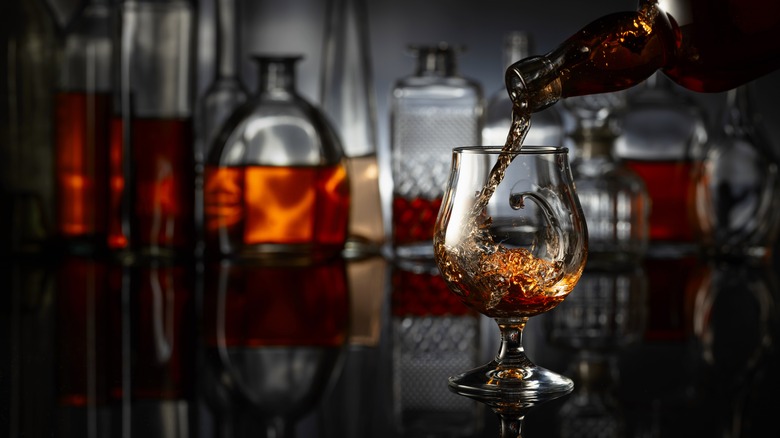 Bottle pouring brady into a cup with several other brandy bottles in the background