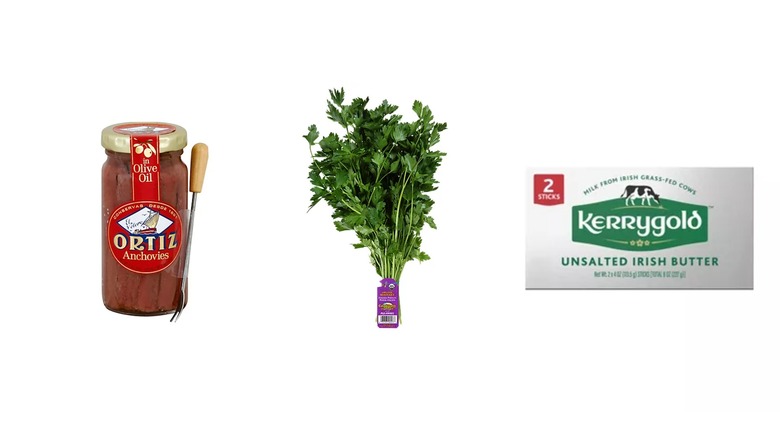 A glass jar of anchovies, a block of Kerrygold unsalted butter, and a bunch of parsley on a white isolated background