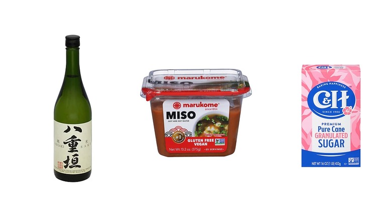 A bottle of sake, container of miso paste, and sugar on a white isolated background