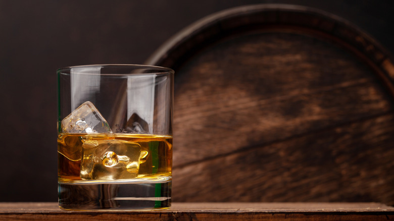 Glass of bourbon on the rocks with a barrel in the background