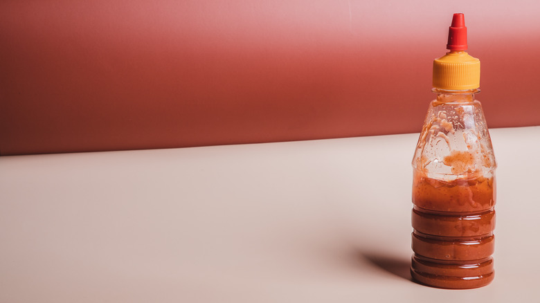 An unmarked bottle of hot sauce on a table with a red background