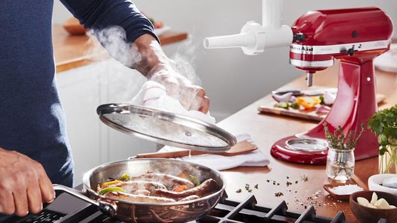 Red KitchenAid mixer with sausage attachment on table with person cooking sausage in pan